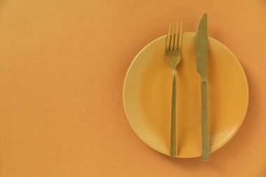 Turuncu arka planda şık bir tabak ve çatal bıçak takımı. Metin için boşluk