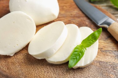 Ahşap masada fesleğen ve bıçakla mozzarella peyniri kes, yakın plan.