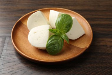 Ahşap masada lezzetli mozzarella peyniri ve fesleğen parçaları, yakın plan.