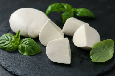 Lezzetli mozzarella peyniri ve fesleğen parçaları karanlık masada, yakın plan.