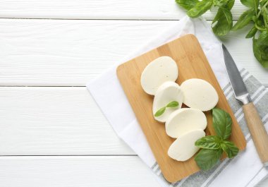 Lezzetli mozzarella peyniri parçaları, fesleğen yaprakları ve beyaz ahşap masa üzerinde bıçak, düz yatak. Metin için boşluk