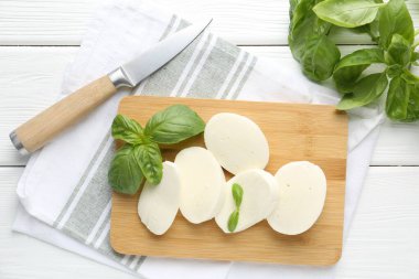 Lezzetli mozzarella peyniri parçaları, fesleğen yaprakları ve bıçak beyaz ahşap masa, düz yatıyordu.