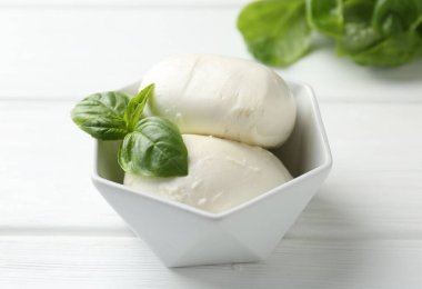 Lezzetli mozzarella peyniri ve fesleğen parçaları beyaz ahşap masada, yakın plan.