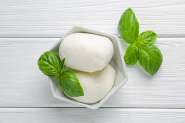 Lezzetli mozzarella peyniri ve fesleğen parçaları beyaz ahşap masada, düz yatıyordu.