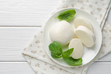 Beyaz ahşap masa üzerinde lezzetli mozzarella peyniri ve fesleğen parçaları.