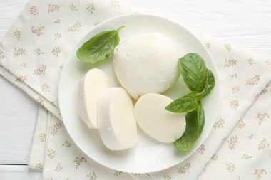 Beyaz ahşap masa üzerinde lezzetli mozzarella peyniri ve fesleğen parçaları.