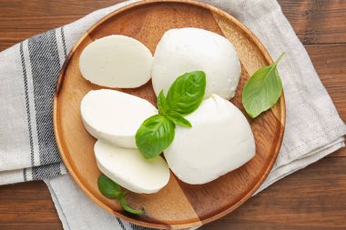 Lezzetli mozzarella peyniri ve fesleğen yaprakları ahşap masanın üstünde.