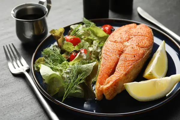 Deniz ürünleri. Siyah masada salata ve limonla servis edilen lezzetli somon bifteği.