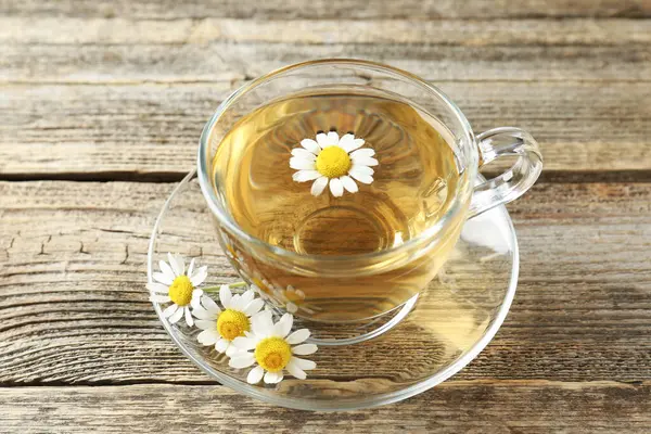 Cam bardakta nefis papatya çayı ve ahşap masada taze çiçekler.