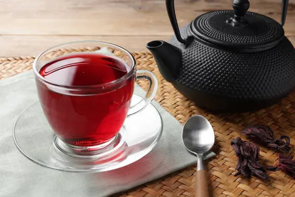 Cam fincanda lezzetli amber çayı, çaydanlık, kuru roselle sepals ve tahta masada kaşık, yakın çekim.