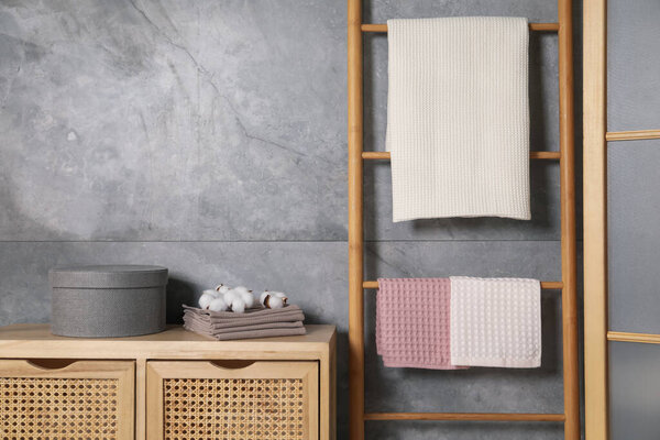 Clean waffle towels, wooden rack and dresser near grey wall in bathroom