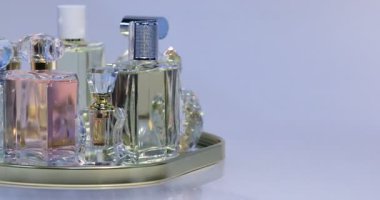 Açık mor arka planda dönen tepside birçok farklı parfüm şişesi, yakın plan. Metin için boşluk