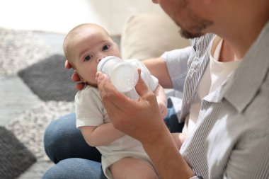 Babası evdeki kanepede bebeğini biberonla besliyor.