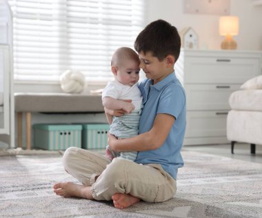 Evde yerde kucaklaşan sevimli küçük kardeşler.