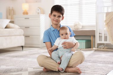 Evde yerde oturan sevimli küçük kardeşler.