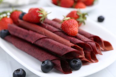 Lezzetli meyve dürümleri, çilekler ve yaban mersinleri beyaz masada, yakın plan.