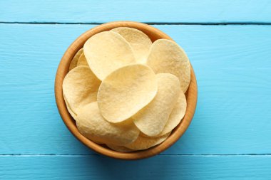 Açık mavi ahşap masada, tabakta patates cipsi.