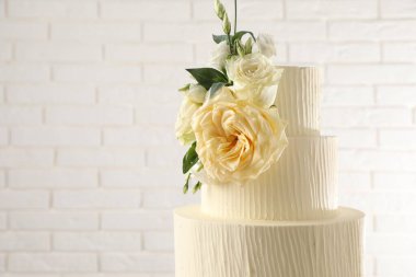 Beyaz tuğla duvarın yanında çiçeklerle süslenmiş nefis düğün pastası, yakın plan. Metin için boşluk