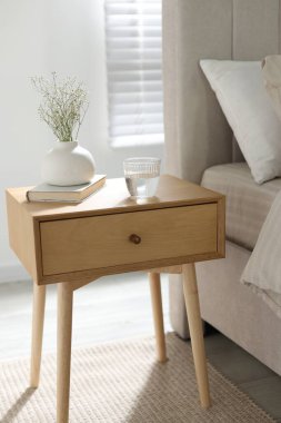 Komodinin yanında vazoda çiçekler, bir bardak su ve yatağın yanında kitap.