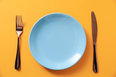 Turuncu arka planda şık bir tabak ve çatal bıçak takımı.