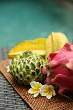 Yüzme havuzunun yakınındaki hasır masada farklı bir tropikal meyve. Metin için boşluk