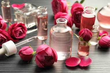 Aromatik esanslı parfüm şişelerini aç ve gri ahşap masada güller, yakın plan.