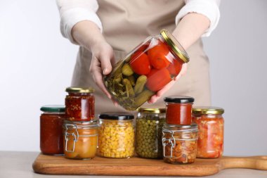 Açık gri arka planda farklı turşulu ürünlerle dolu kavanozları olan kadın, yakın plan.