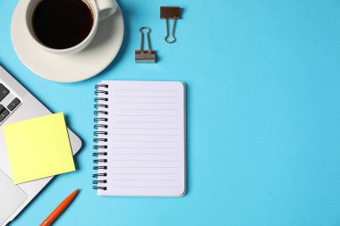 Not defteri, yapışkan not, kalem, cilt klipleri, açık mavi arka planda kahve ve dizüstü bilgisayar, düz. Metin için boşluk