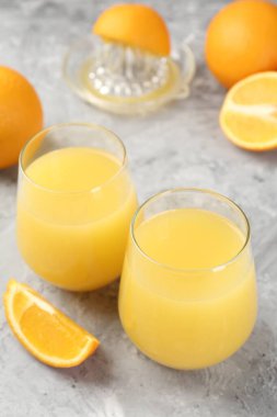 Portakal suyu bardakta, taze meyve suyu ve meyve sıkacağı gri masada, yakın plan.