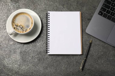 Defter, kalem, kahve ve dizüstü bilgisayar gri masada, düz yerde.