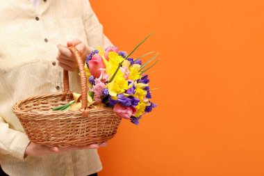 Turuncu arka planda güzel çiçekleri olan hasır sepetli bir kadın, yakın plan. Metin için boşluk