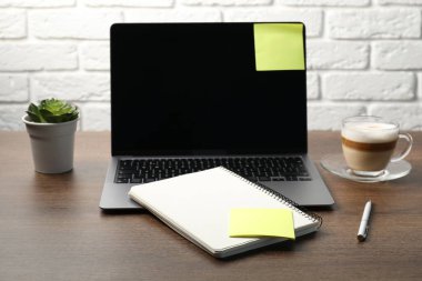 Yapışkan notlu dizüstü bilgisayar, defter, kalem, kahve ve bitki ahşap masaya.