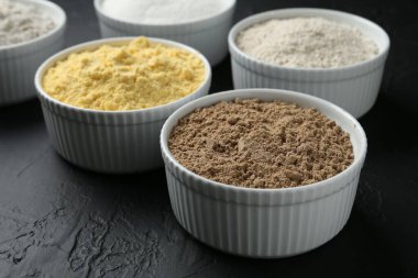 Siyah desenli masa üzerindeki kaselerde farklı un türleri, yakın plan.