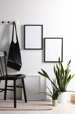 Beyaz duvarda boş resim çerçeveleri, ip torbası, sandalye ve ev bitkileri