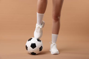 Bej arka planda futbol topu olan spor ayakkabılı kadın, yakın plan.