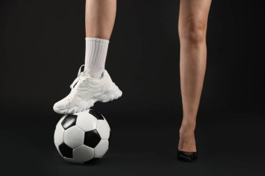 Arka planda futbol topu olan yüksek topuklu ayakkabılı ve spor ayakkabılı bir kadın.