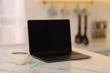 Boş ekranlı dizüstü bilgisayar, bir fincan sıcak içecek ve mutfaktaki beyaz mermer masaya kalem. Tasarım için model