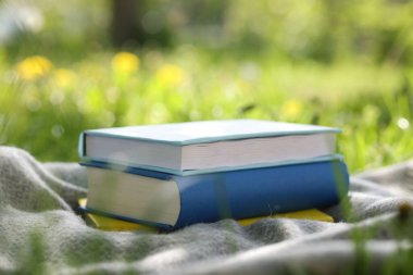 Yığınla kitap ve battaniye dışarıda yeşil çimlerin üzerinde, yakın plan.