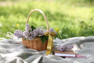 Yığınla kitap ve hasır sepet. Yeşil çimlerin üzerinde leylak çiçekleri.