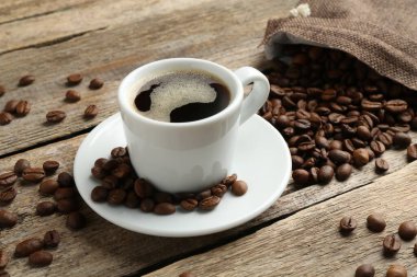 Aromatik kahve fincanda ve fasulyeler ahşap masada, yakın plan.