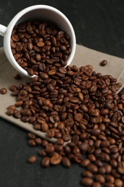 Aromatik kahve çekirdekleri ve siyah masada ters çevrilmiş fincanlar, yakın plan.