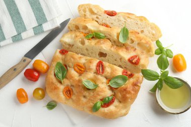 Domates, fesleğen, yağ ve bıçakla nefis Focaccia 'yı ışık masasında düz bir şekilde kes.