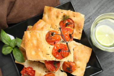 Domatesli, baharatlı ve gri masadaki bir bardak suyla nefis Focaccia parçaları.