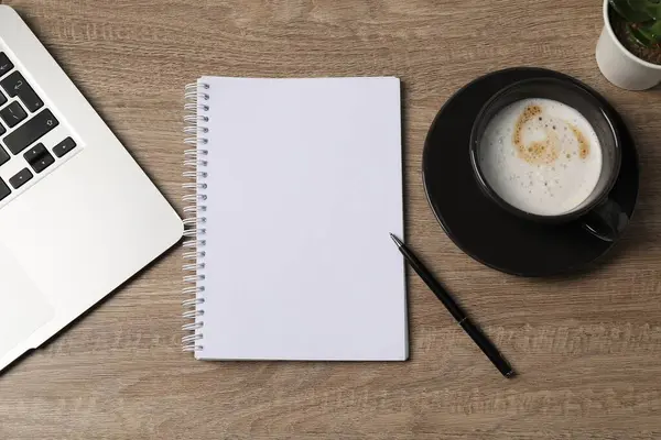 Defter, kalem, kahve ve dizüstü bilgisayar ahşap masada, düz yatıyordu.
