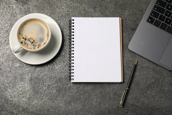 Defter, kalem, kahve ve dizüstü bilgisayar gri masada, düz yerde.