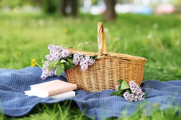 Yığınla kitap, battaniye ve hasır sepet. Yeşil çimlerin üzerinde leylak çiçekleri, yakın plan.
