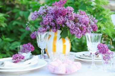 Güzel leylak çiçekleri, zephyrler, tabaklar, çatal bıçak takımı ve bardaklar bahçede, yakın plan.