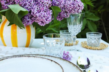 Güzel leylak çiçekleri, tabaklar, kaşık, bardaklar ve mumlar bahçede, yakın plan