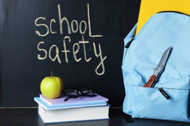 Sırt çantasında bıçak, kitap, defterler, bardaklar ve elma tahtaya yakın siyah tahta masada. Okul güvenliği