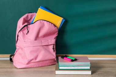 Çalışma kitapları, defterler, kitap ve fosforlu kalemler karatahtanın yanındaki tahta masada, metin için yer var.